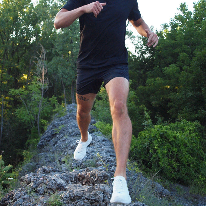 Justis Faulkner wearing black Mentality Shorts while running on a rock trail in a wooded area